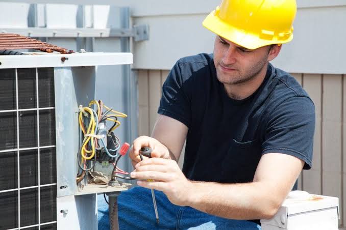 Technician repairing wiring inside an outdoor HVAC condenser