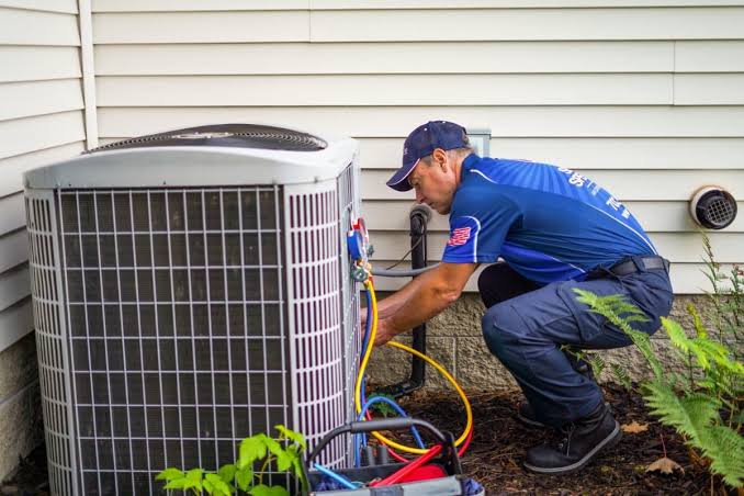 HVAC technician servicing a residential condenser beside a home