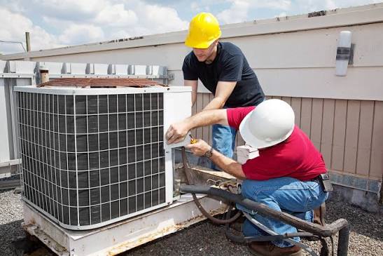Two HVAC technicians servicing a rooftop cooling unit